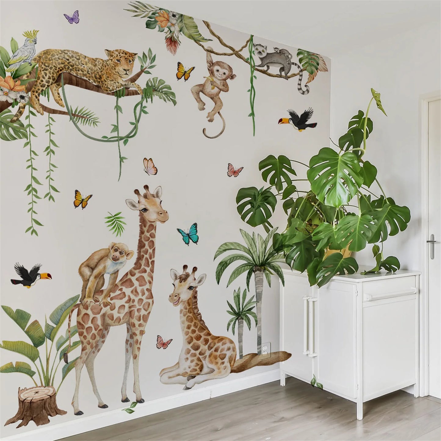 Woodland Animal Wall Decals decorate a playroom, featuring giraffes, monkeys, and a leopard amidst plants and butterflies.