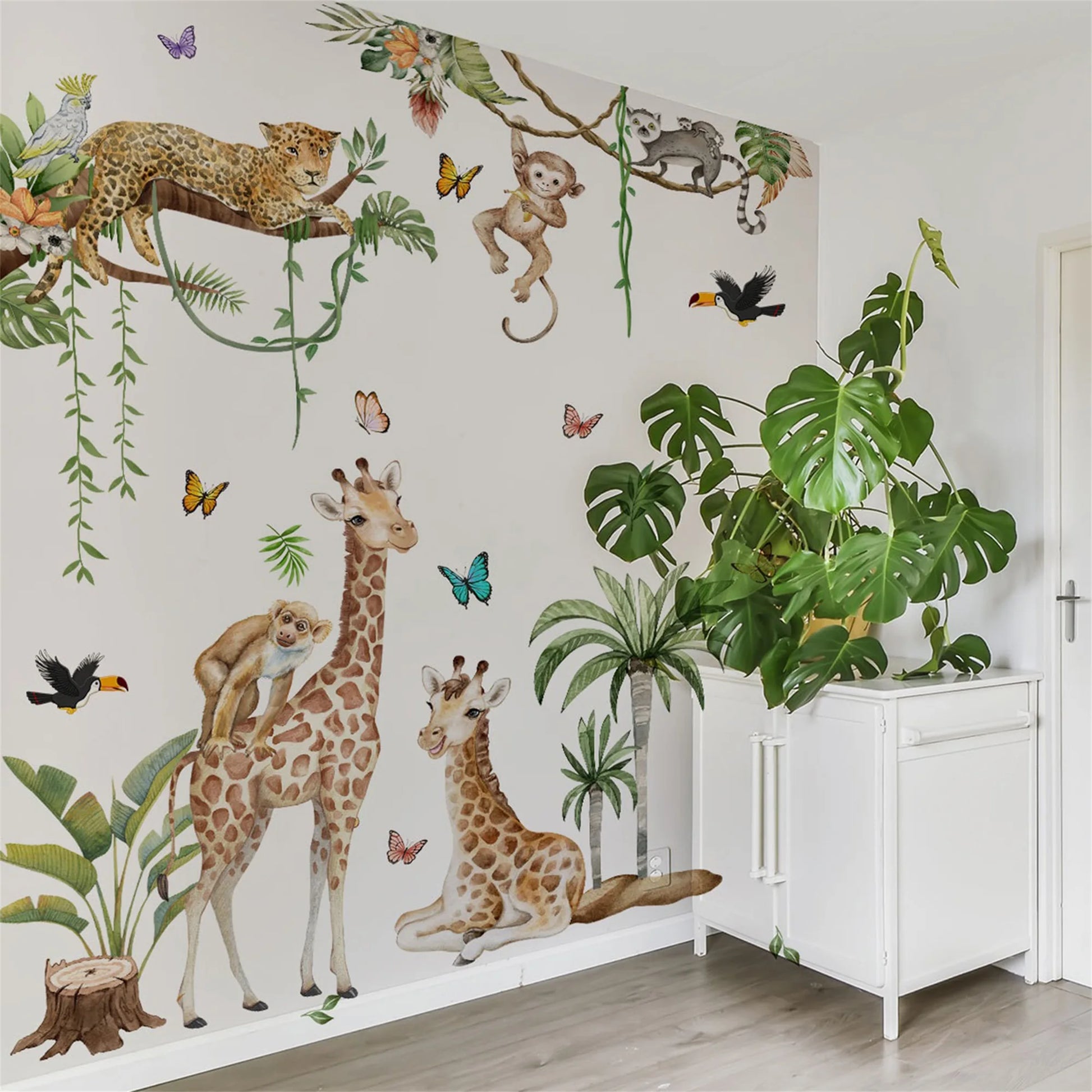 Woodland Animal Wall Decals decorate a playroom, featuring giraffes, monkeys, and a leopard amidst plants and butterflies.